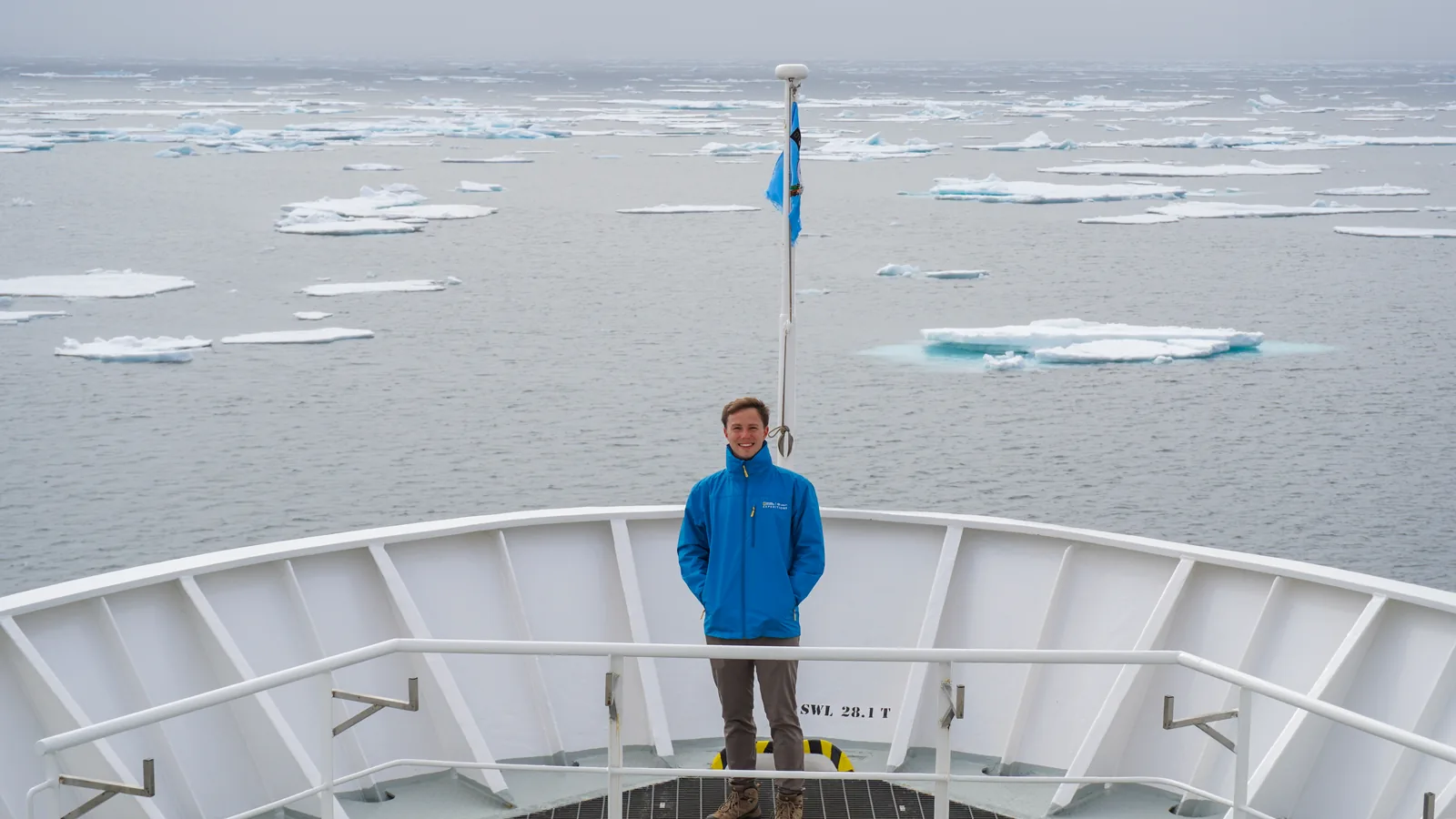 Sam standing on the bow of an expedition ship surrounded by Arctic sea ice